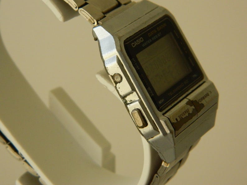 May include: A silver Casio Data Bank watch with a black digital display. The watch has a silver metal band and a black face with white lettering. The watch is in good condition, but shows signs of wear.