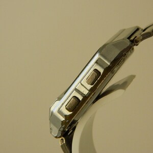 May include: A silver-toned wristwatch with a square face and a metal band. The watch has two buttons on the side of the case.