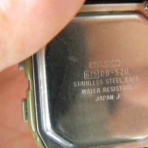 May include: Close-up of the back of a silver Casio watch with the text "CASIO 675 DB-520 STAINLESS STEEL BACK WATER RESISTANT JAPAN J" engraved on the back.