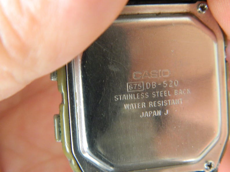 May include: Close-up of the back of a silver Casio watch with the text "CASIO 675 DB-520 STAINLESS STEEL BACK WATER RESISTANT JAPAN J" engraved on the back.