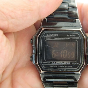 May include: Black Casio digital watch with a black metal band. The watch face displays the time, date, and has buttons for alarm, chronograph, light, and mode. The watch is water resistant to 5 bar.
