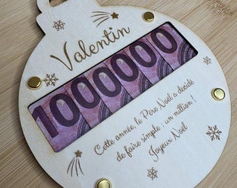 Peut inclure: Une décoration de Noël ronde en bois avec un ruban rouge, portant le prénom Valentin, le nombre 1000000 et le texte : Cette année, le Père Noël a décidé de faire simple : un million ! Joyeux Noël, agrémentée de gravures de flocons.