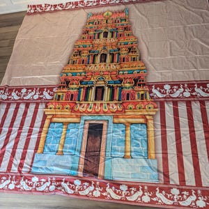 Puede incluir: Un tapiz de tela grande que presenta una ilustraci&oacute;n central de una colorida torre de templo hind&uacute; gopuram. El dise&ntilde;o incluye un fondo beige claro con rayas verticales rojas en la parte inferior y un borde decorativo de pavos reales blancos sobre rojo.