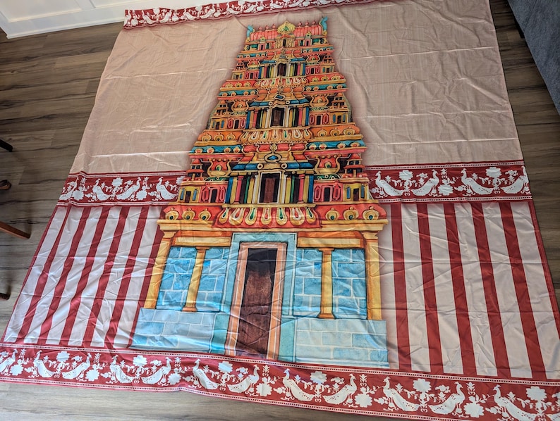 Puede incluir: Un tapiz de tela grande que presenta una ilustraci&oacute;n central de una colorida torre de templo hind&uacute; gopuram. El dise&ntilde;o incluye un fondo beige claro con rayas verticales rojas en la parte inferior y un borde decorativo de pavos reales blancos sobre rojo.