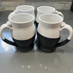 May include: Set of four ceramic mugs with a black and white design. Each mug has a white top and a black bottom.