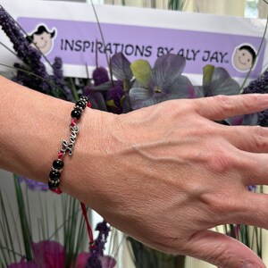 May include: A red string bracelet with black beads and a silver charm that says "Love".