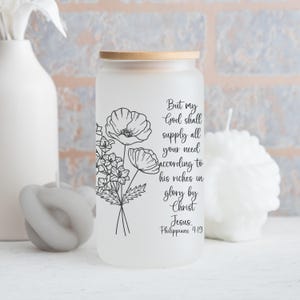 May include: A frosted glass tumbler with a bamboo lid featuring a black line art illustration of a floral bouquet and the text: But my God shall supply all your need according to his riches in glory by Christ Jesus. Philippians 4:19.