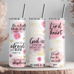 May include: Three white stainless steel tumblers with silver straws. Each tumbler features inspirational quotes and floral designs in pink and gold. The quotes include "Be a light", "God is within her", and "Trust in the Lord".
