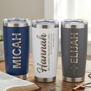 May include: Three stainless steel travel tumblers with silver rims and lids. One is navy blue with "MICAH" in silver, another is white with "Hannah" and a Bible verse, and the third is gray with "ELIJAH" and a cross.