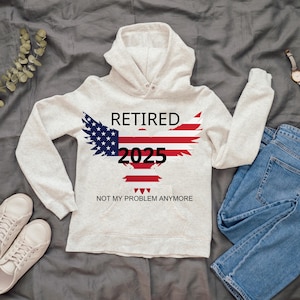 Peut inclure: Un sweat à capuche gris clair avec le mot "RETIRED" au-dessus d'un aigle aux couleurs du drapeau américain. L'année "2025" est imprimée en dessous, avec la phrase "NOT MY PROBLEM ANYMORE" en dessous.