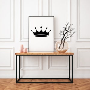 May include: A framed art print featuring a black crown design on a white background. The artwork is displayed on a wooden console table with a black metal frame, alongside decorative vases and a glass bowl with branches.
