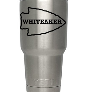 May include: A stainless steel YETI tumbler with a black arrowhead design and the name "WHITEAKER" printed on it.
