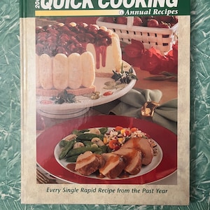 May include: A cookbook titled "Taste of Home's Quick Cooking Annual Recipes 2001" with a photo of a dessert and a plate of food on the cover. The dessert is a layered dessert with a red sauce and a white filling. The plate of food contains a pork tenderloin with a brown sauce, green beans, and rice.