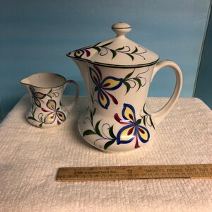 May include: A white ceramic creamer and sugar set with a butterfly design. The creamer and sugar are decorated with blue, yellow, red, and green butterflies.