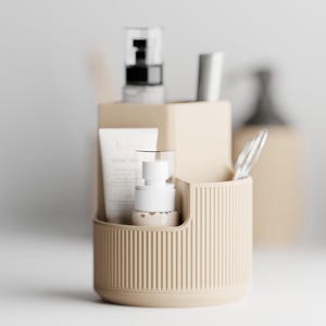 Op de afbeelding: Een beige, geribbelde, cilindrische organizer met huidverzorgingsproducten. De organizer bevat een tube lotion, een witte pompflacon en andere cosmetische items. De achtergrond bevat extra beige containers en vage items.