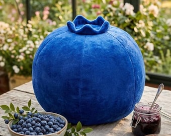May include: A large, round, plush blueberry-shaped pillow with a vibrant blue, soft-textured fabric surface. The top of the plush features a distinct, ruffled crown detail characteristic of a fresh blueberry, creating a rounded, stuffed fruit form.