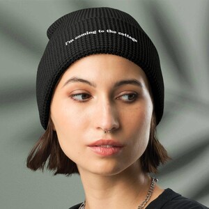Puede incluir: Gorro negro con el texto blanco "I'm coming to the cottage". El gorro está hecho de un material de punto acanalado. La persona de la imagen lleva una camiseta negra y un collar de cadena plateada.