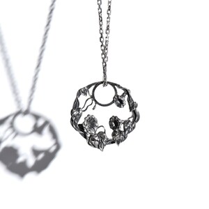 May include: A silver necklace with a delicate pendant featuring a circular design of intertwining vines and flowers.