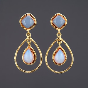 May include: Gold dangle earrings with two teardrop-shaped stones. The top stone is a light blue square and the bottom stone is a white teardrop.
