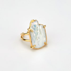 Puede incluir: Un anillo de oro con una perla grande, blanca e irregular en el centro.