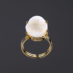 Puede incluir: Un anillo de oro con una piedra preciosa de ágata blanca. La piedra preciosa es una geoda con una textura cristalina.