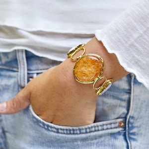 May include: A gold bracelet with a large, oval-shaped, orange gemstone. The bracelet has a delicate, chain-like design.