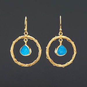 May include: Gold hoop earrings with a dangling turquoise blue gemstone in the center of each hoop.