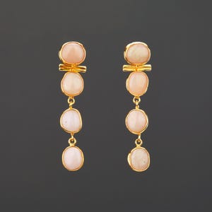Pode incluir: Um par de brincos de ouro com três pedras ovais cor-de-rosa penduradas em cada brinco.