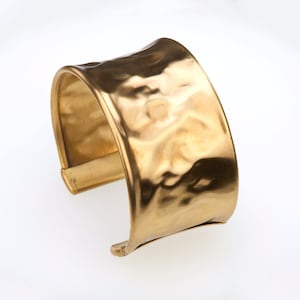 May include: A gold-toned metal cuff bracelet with a hammered texture.