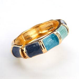 May include: A gold-toned hinged bracelet with rectangular enamel segments in shades of blue and teal. The bracelet has a textured gold finish on the inside and a clasp closure. The enamel segments have a marbled appearance.
