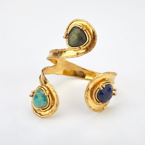 May include: Gold-toned bracelet with a twisted design and three different colored gemstones. The stones are a dark green, a light blue, and a teal green.