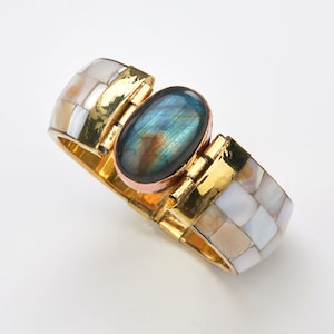 May include: A gold and white bangle bracelet with a large oval-shaped iridescent blue gemstone set in the center.