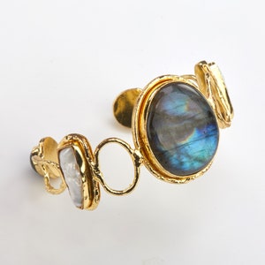 May include: Gold cuff bracelet with a large oval blue labradorite gemstone and two smaller white pearl accents.