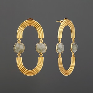 May include: A pair of gold-tone earrings featuring two stacked, ribbed arch-shaped metal components connected by two round, faceted, translucent grey stones. The earrings have a post-back closure and a polished metallic finish.