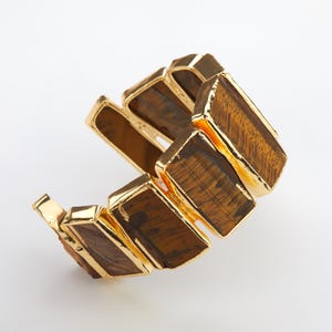 May include: A gold bracelet with a tiger's eye stone design. The bracelet is made of multiple rectangular pieces of tiger's eye stone, each with a gold trim.