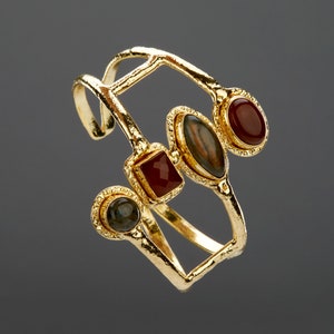 May include: Gold bangle bracelet with four gemstones. The bracelet has a geometric design and features a red, a green, and two brown gemstones.