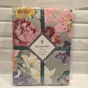 May include: A packaged Waterford Linens floral print textile. The design features large pink, yellow, and burgundy flowers on a gray background. The packaging includes a label with the brand name and product details.
