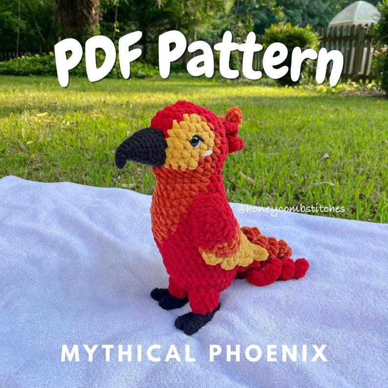 May include: A crocheted phoenix in shades of red, orange, and yellow, with a black beak and feet. The text "PDF Pattern" and "Mythical Phoenix" are displayed. The phoenix is set against a green grassy background.