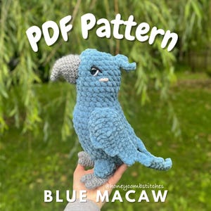 May include: A handmade blue crochet macaw bird with a gray beak and feet. The text "PDF Pattern" is at the top, and "BLUE MACAW" is at the bottom. The bird is held in front of a blurred green background.