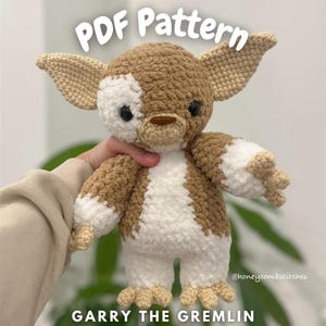 May include: A crocheted plush toy of "Garry the Gremlin" with brown, white, and tan yarn. The toy has large ears, black eyes, and a white patch on its face. The text "PDF Pattern" and "Garry the Gremlin" are displayed.