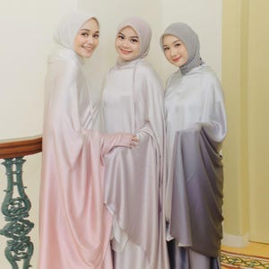 May include: Three women wearing long, flowing robes with matching headscarves. The robes are a gradient of pink, gray, and purple.