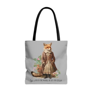 May include: A gray tote bag with a fox wearing a brown jacket and a white dress. The fox is standing in a field of flowers. The text "Like a fox in the woods. Be sly and stylish!" is printed on the bottom of the bag.