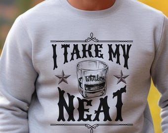 Może przedstawiać: Szara bluza z nadrukiem "I take my whiskey neat" w stylu vintage. Tekst jest otoczony ozdobnymi elementami i gwiazdami. W środku tekstu znajduje się rysunek szklanki whisky.