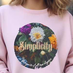 Puede incluir: Sudadera rosa con un diseño circular de estampado floral. El círculo presenta una variedad de flores y hojas, y el texto "Simplicity is the keynote of all true elegance."