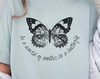May include: A light blue t-shirt with a black and white butterfly graphic and the text "In a world of moths, be a butterfly".