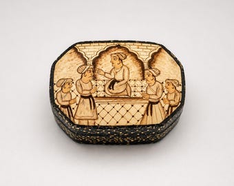 Pode incluir: Caixa octogonal pintada à mão, com exterior preto e uma cena detalhada na tampa. A tampa retrata figuras em trajes tradicionais, envolvidas numa conversa. A obra de arte é em tons de castanho e bege, com padrões intrincados.