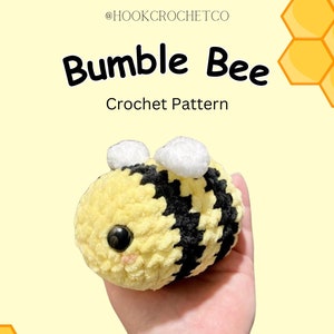 Peut inclure: Un jouet abeille bourdon crocheté avec des rayures noires et jaunes, des ailes blanches et un visage mignon. L'abeille est tenue dans une main sur un fond jaune avec des motifs de nid d'abeille.