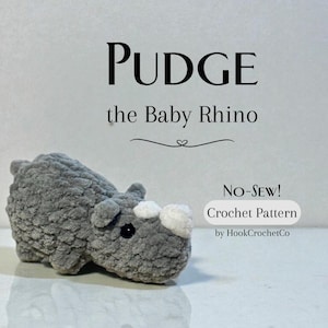 May include: A gray crocheted rhino toy labeled "Pudge the Baby Rhino." The no-sew crochet pattern is by HookCrochetCo. The rhino has a white patch on its snout and small black eyes. The toy is made of a soft, plush material.