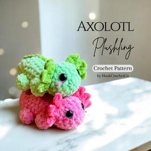 May include: Two crocheted axolotl plushies, one green and one pink, stacked on top of each other. The plushies have large black eyes and frilly gills. The image includes the text "AXOLOTL Plushling Crochet Pattern by HookCrochetCo."