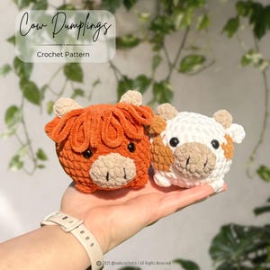 May include: Two plush crochet cow dumplings, one in solid orange with a beige snout and the other in white with brown patches and a beige snout. Both feature small horns and black eyes. The text Cow Dumplings Crochet Pattern is visible.